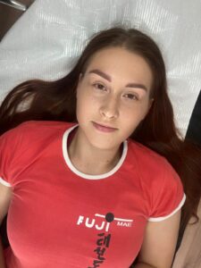 Młoda kobieta leżąca na łóżku zabiegowym, po wykonaniu makijażu permanentego brwi.
